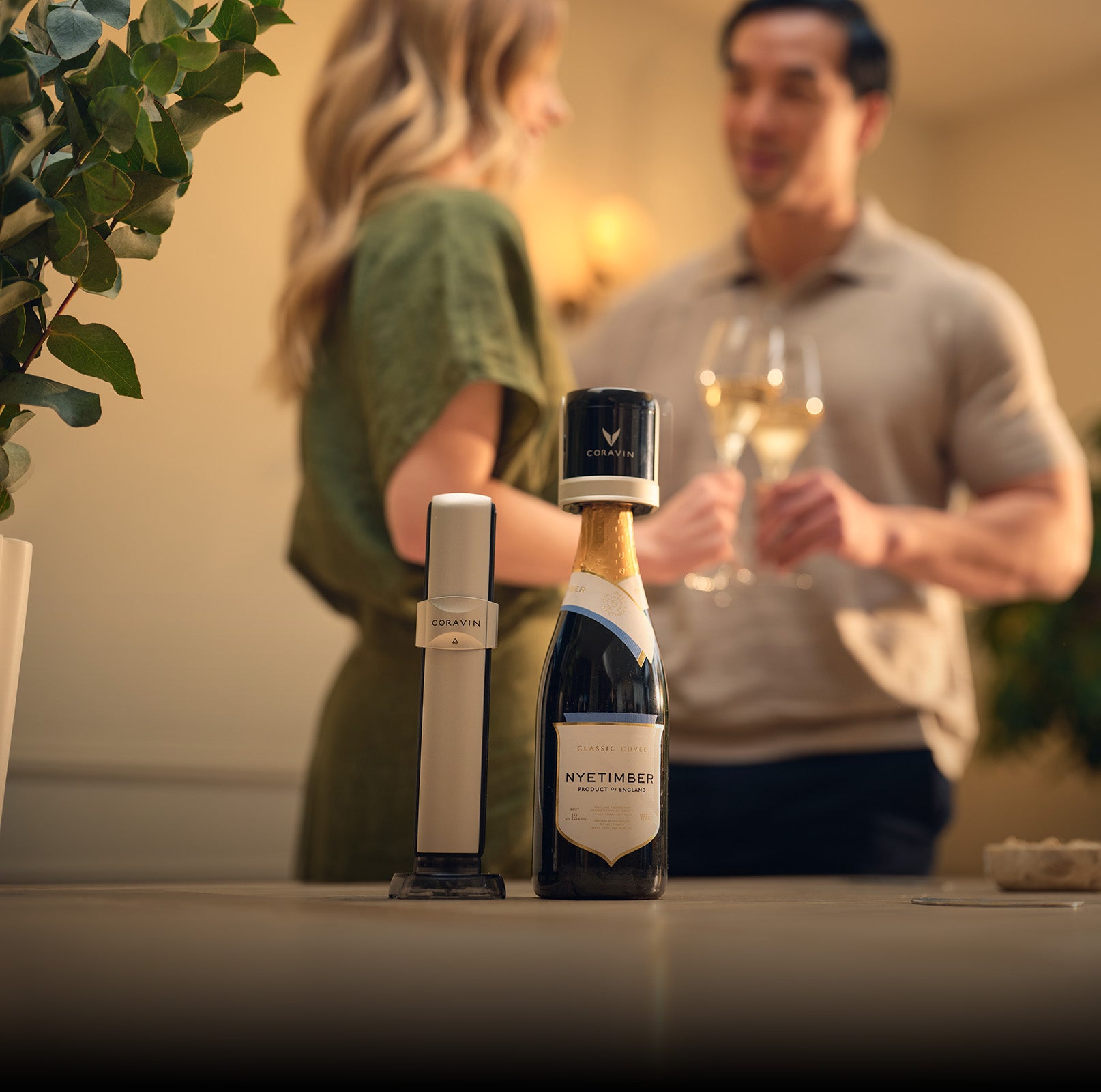 Bottle of Nyetimber champagne with a wine bottle opener on a table, with a blurred couple in the background.